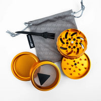 An orange metal herb grinder set with a gray drawstring bag, black plastic fork, and black mesh screen, arranged on a white background.