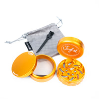 An orange metal herb grinder set shown open on a white background, with a gray drawstring pouch, black cleaning brush, and mesh screen visible. The lid shows the brand name 'Jnglest'.