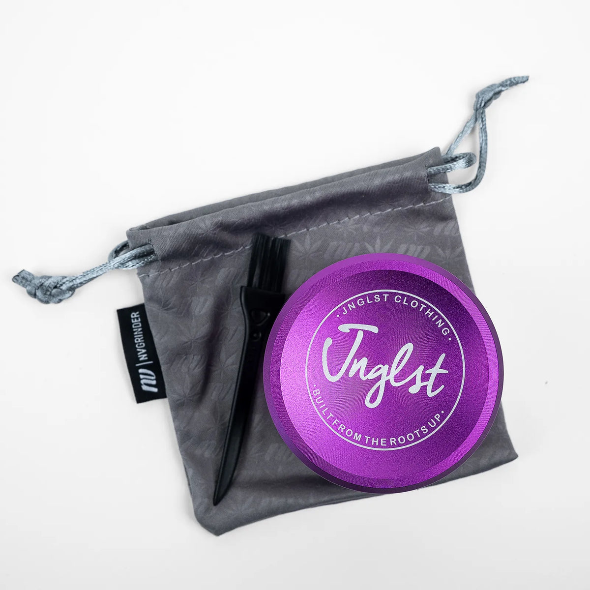 A purple circular metal tin with a black handle and black brush resting on top of a gray drawstring pouch. The pouch has a black tag on the left side with the brand name 'Inglester'.