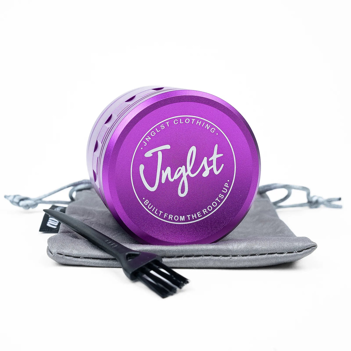 A purple metal herb grinder with a white printed logo, resting on a gray drawstring pouch with a black cleaning brush, on a white background.