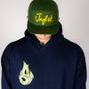 Person wearing a green cap with yellow text and a navy Fire hoodie with a green logo on a plain background