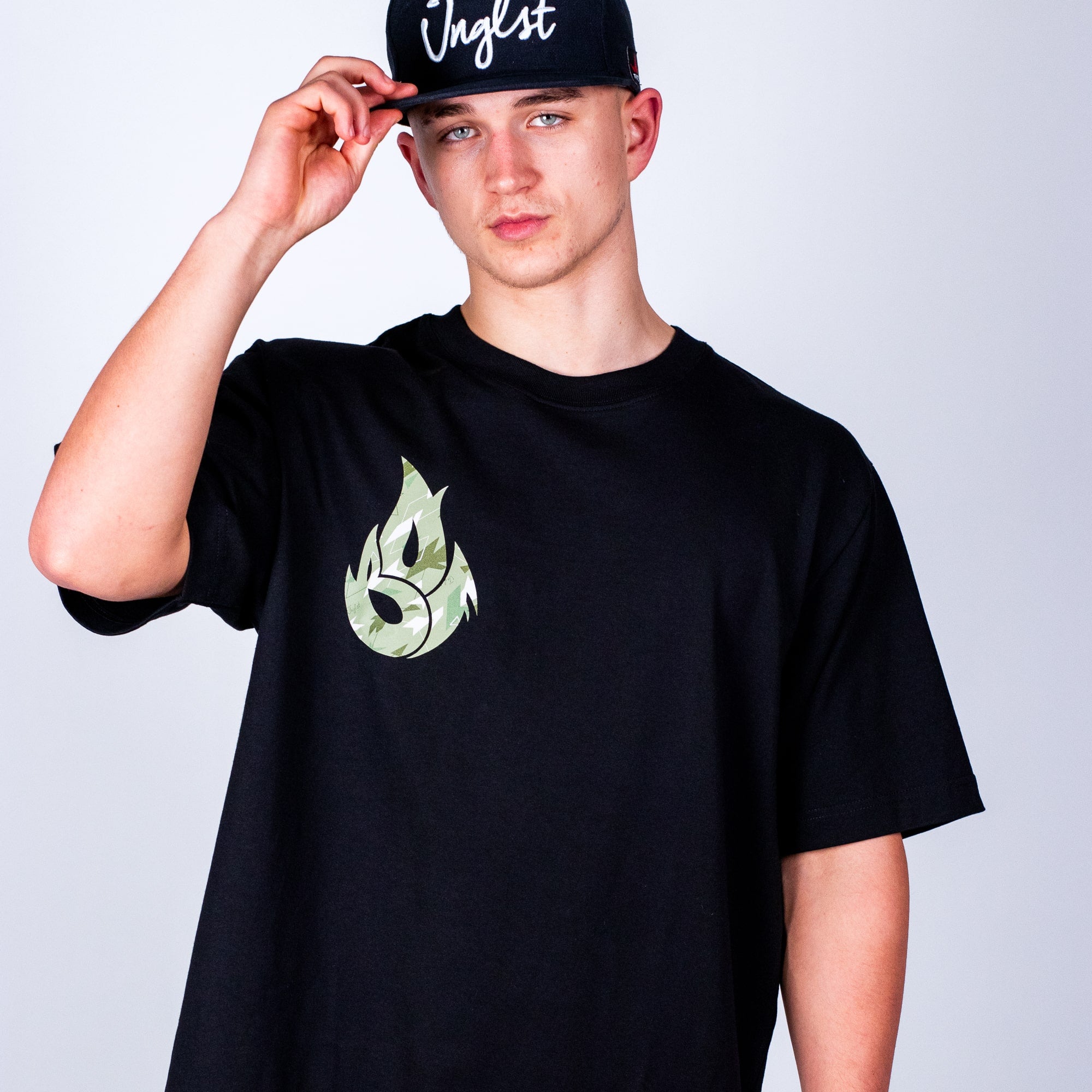 Person wearing a black Born Outta Fire t-shirt with a green logo and a black cap on a light gray background