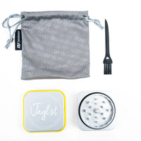 A Jnglst weed grinder kit on a white background, including a gray drawstring pouch with a subtle leaf pattern, a black cleaning brush, a silver metal grinder with a black ring, and a silver lid with a yellow border and the Jnglst logo.