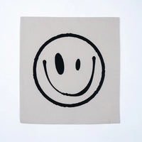 A square canvas print featuring a minimalist black smiley face on a light beige background, displayed against a clean white wall.