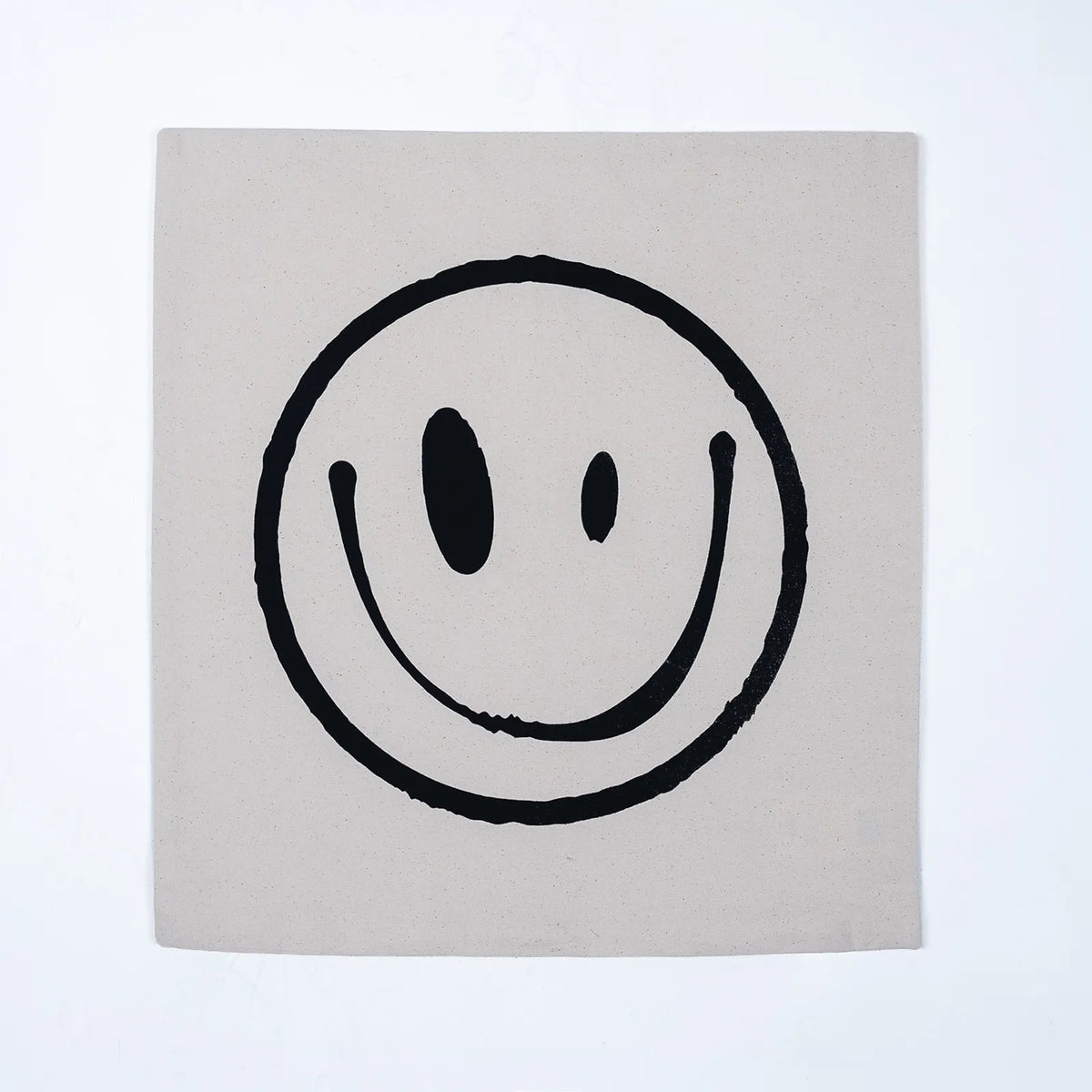 A square canvas print featuring a minimalist black smiley face on a light beige background, displayed against a clean white wall.