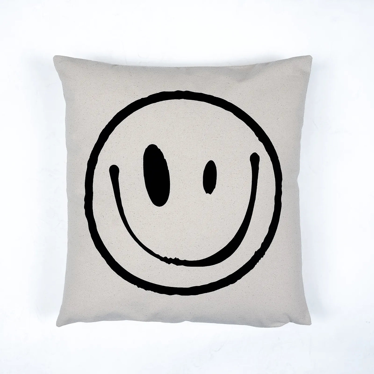 A square throw pillow in a light beige linen fabric featuring a large, hand-drawn black smiley face graphic in the center, set against a clean white background.