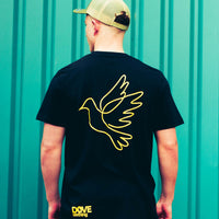 Person wearing a black t-shirt with a yellow dove design on the back, standing against a teal background.