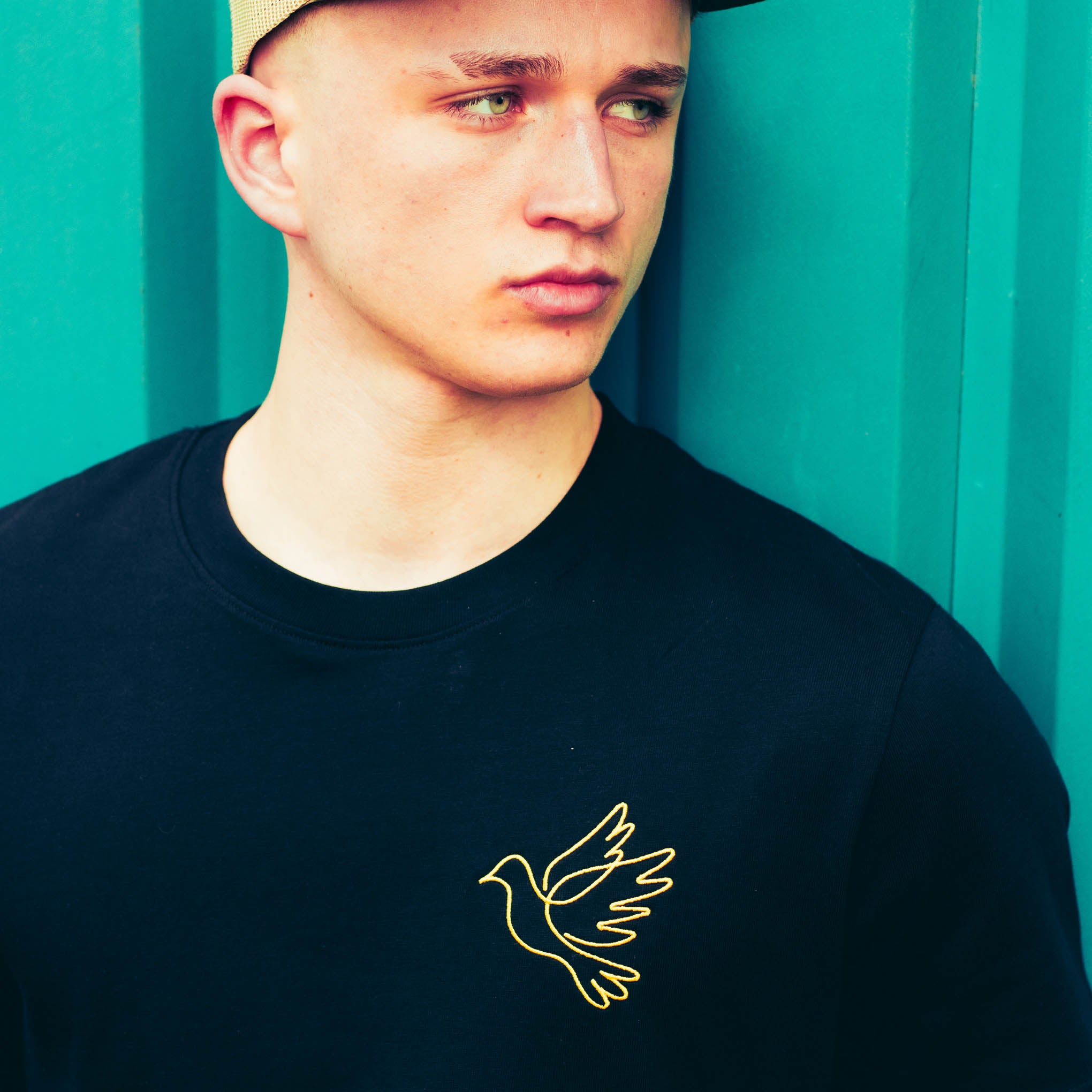 Man wearing a black t-shirt with a yellow dove design against a teal background