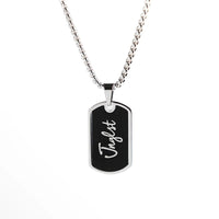 A silver-toned dog tag necklace with a black enamel insert and the name 'Jnglst' in white script, suspended from a silver box chain against a plain white background.