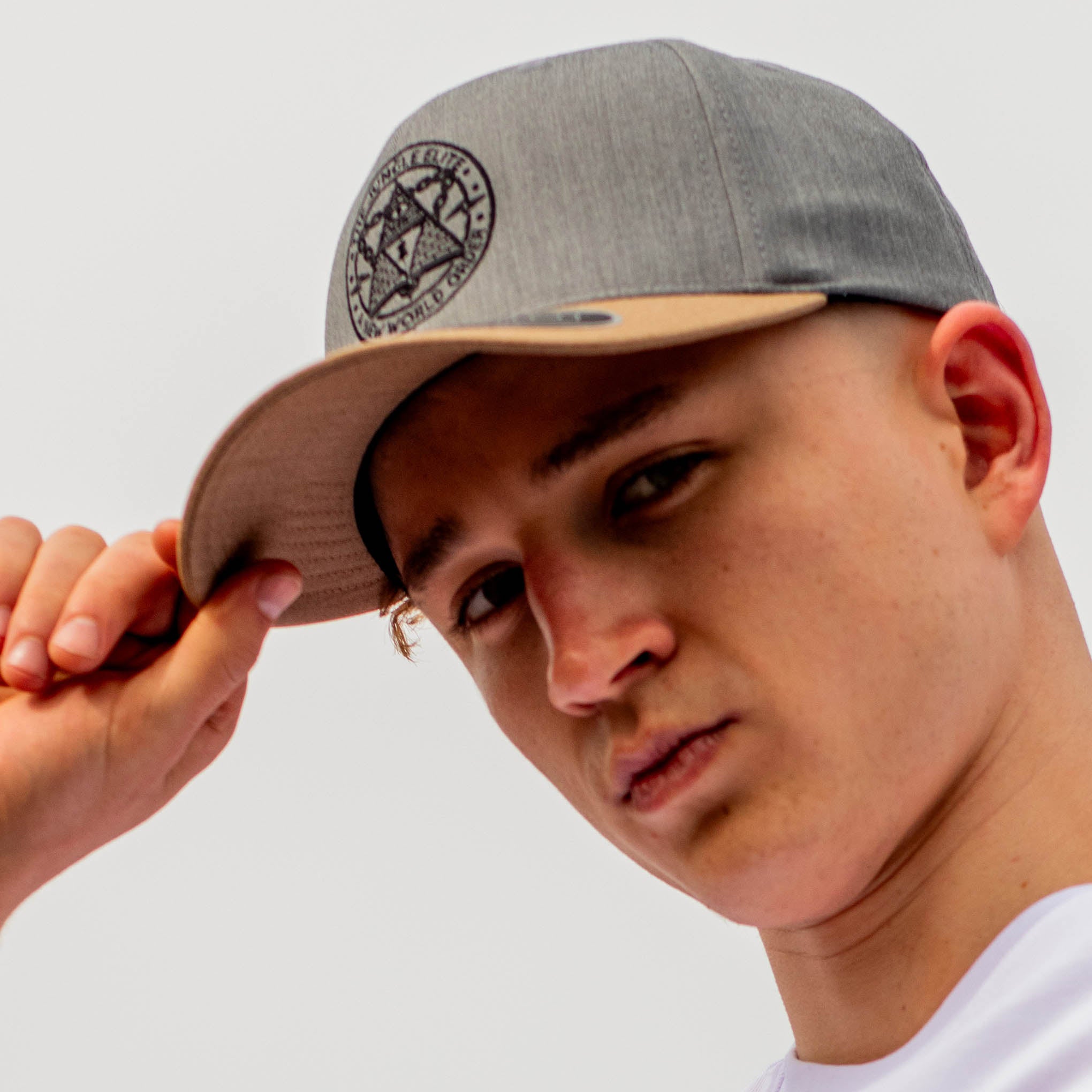 Person wearing a gray and beige cap with a logo, against a plain background