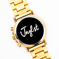 Bronze coloured watch with a black face displaying the word 'Jnglst'.