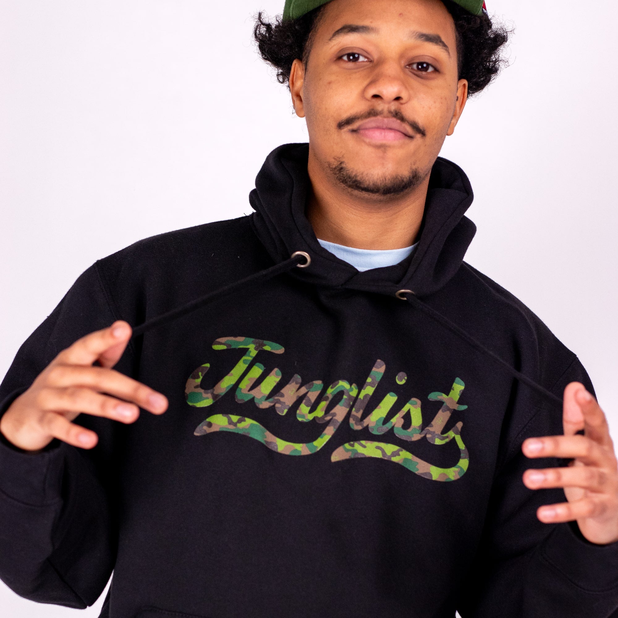 Person wearing a black hoodie with 'Junglist' in camouflage text on a white background
