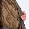 Close-up of a brown quilted Junglist jacket with a hand zipping it up on a white background
