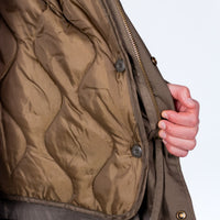 Close-up of a brown quilted Junglist jacket with a hand zipping it up on a white background
