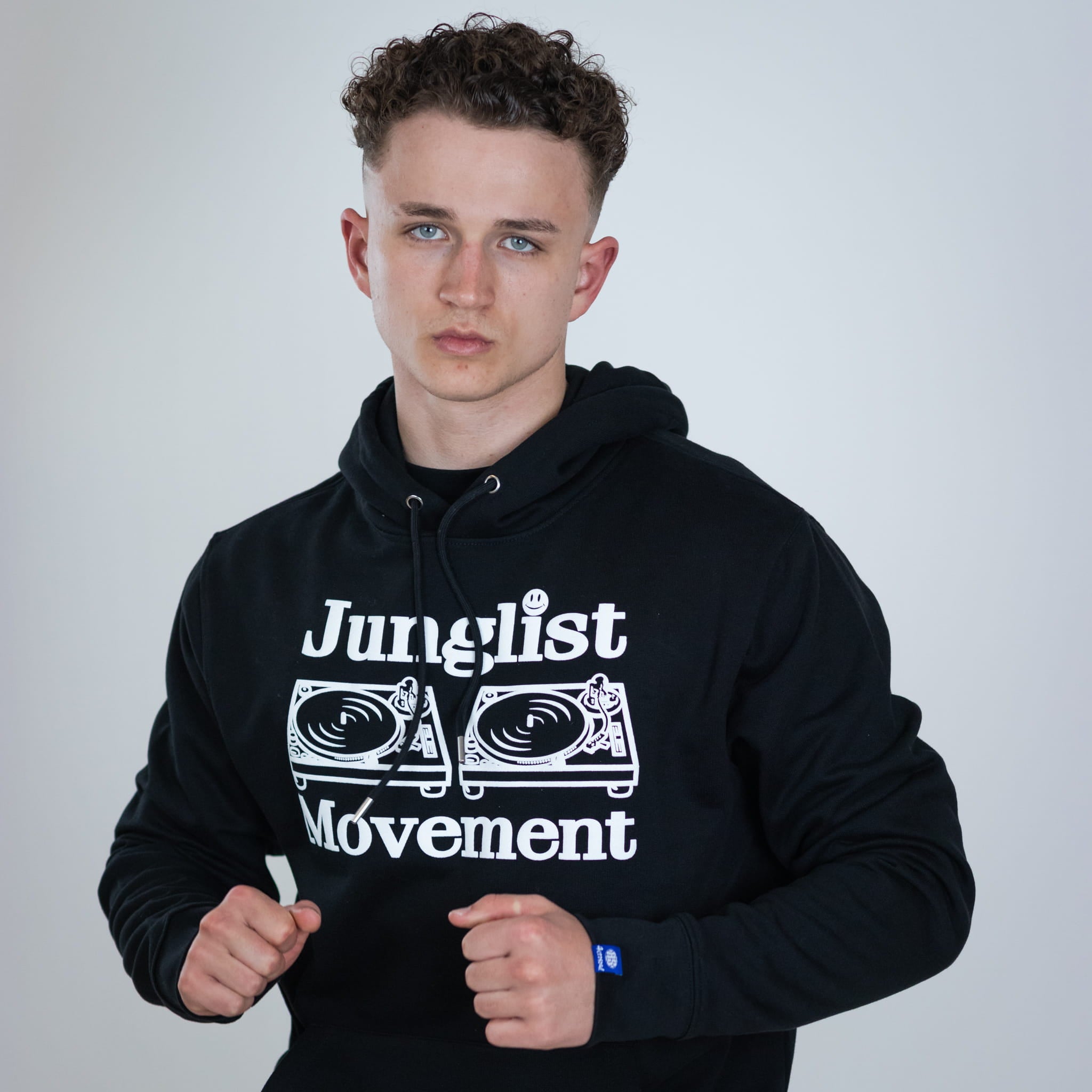 Person wearing a black hoodie with 'Junglist Movement' text and graphics on a plain background