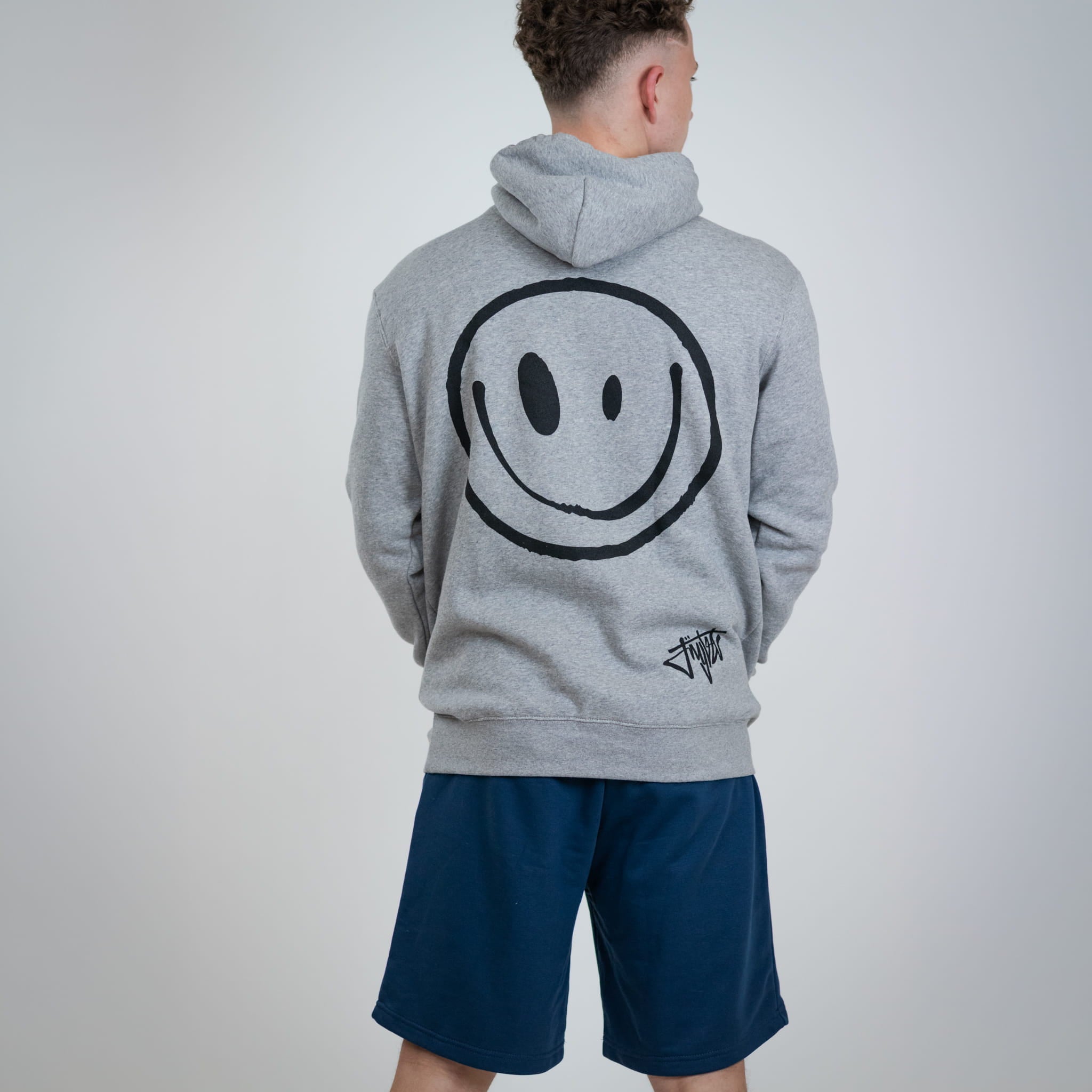 Person wearing a gray hoodie with a smiley face design on the back, standing against a plain background.