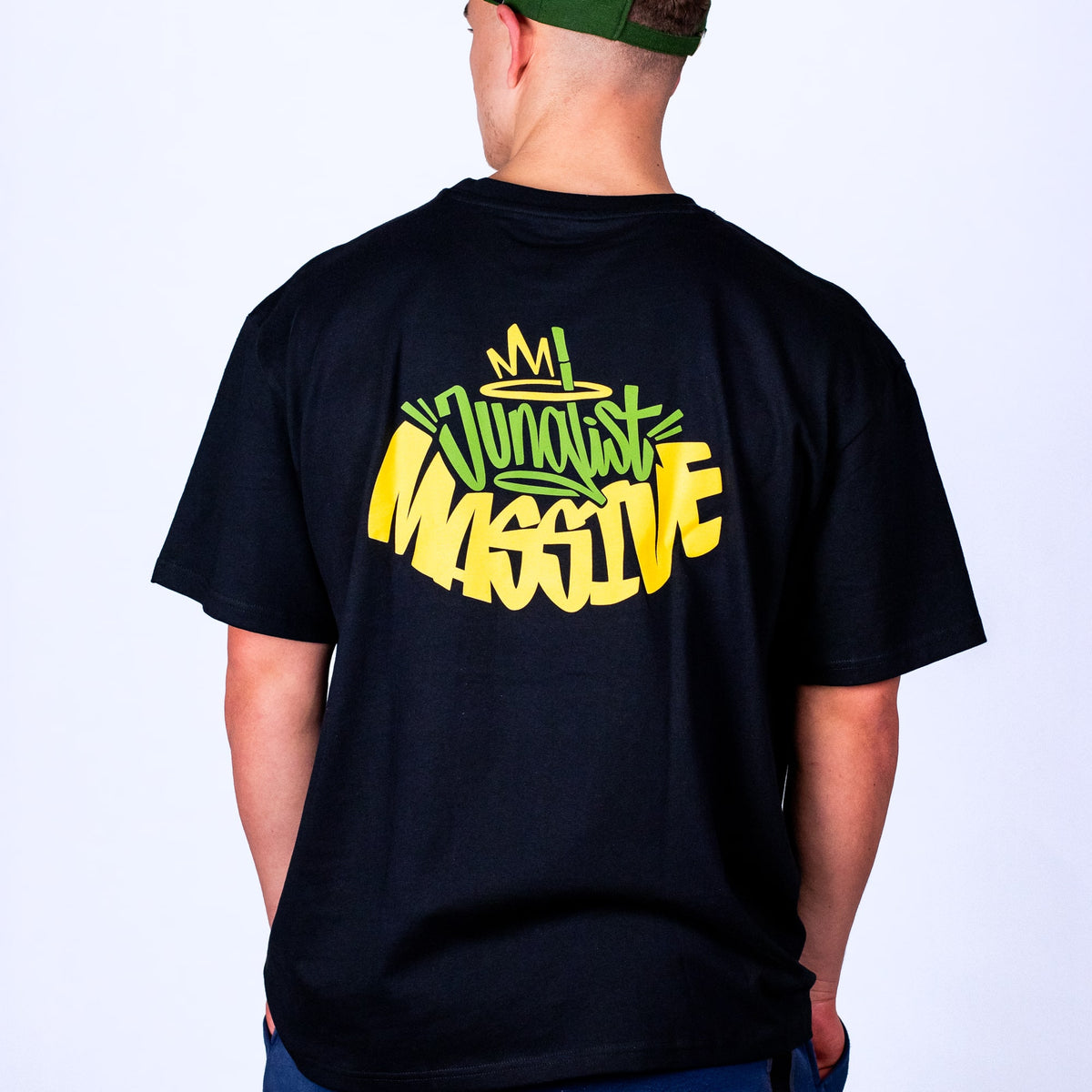 Person wearing a black Junglist Massive t-shirt with colourful text on the back against a plain background