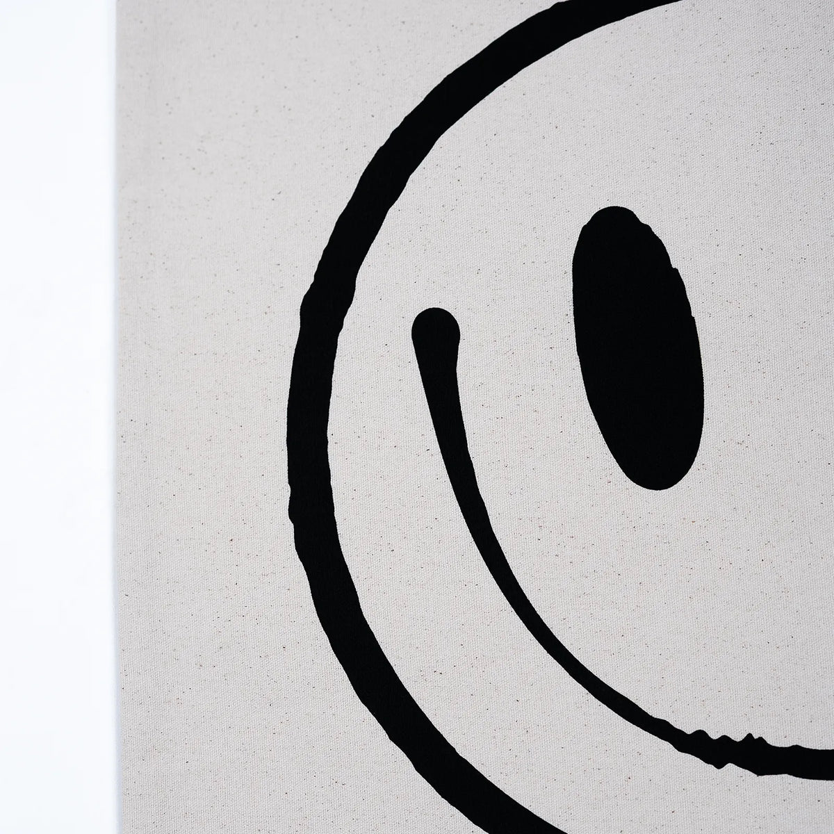 Close-up of a minimalist black smiley face design on a light warm gray textured surface, with a narrow white strip visible along the left edge.