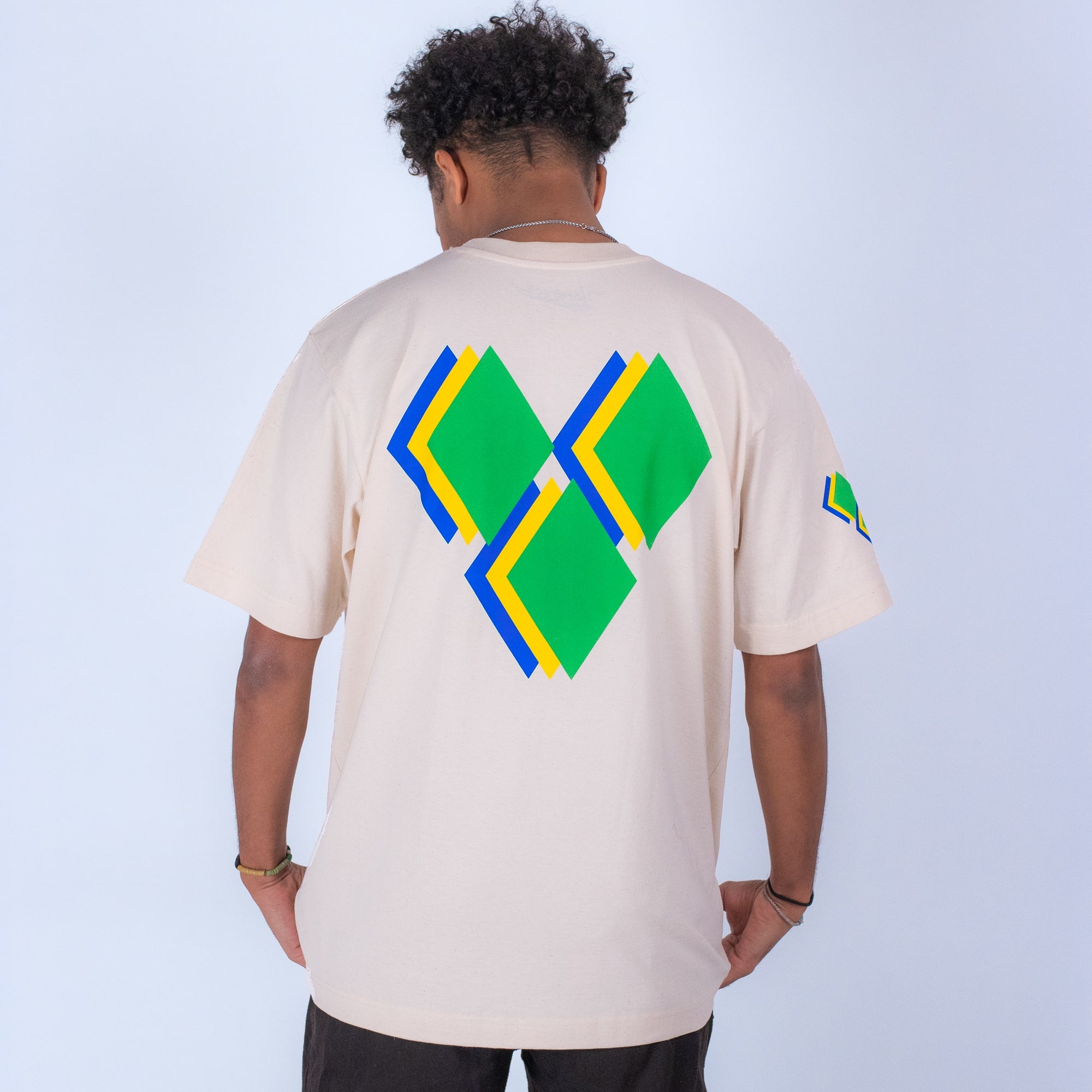 Person wearing a beige t-shirt with geometric yardrock designs on the back and sleeve against a light blue background