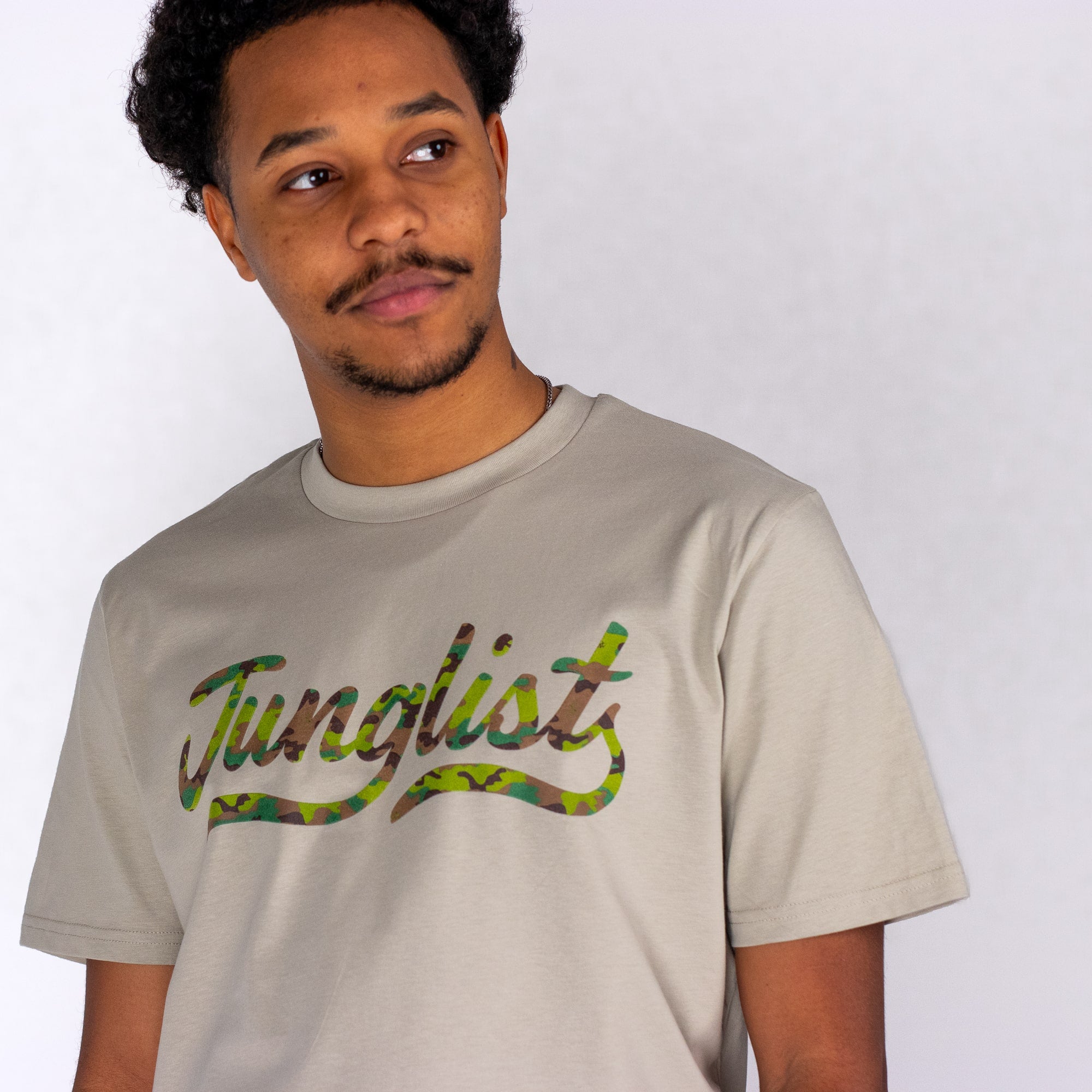 Person wearing a beige t-shirt with 'Junglists' printed on it against a white background