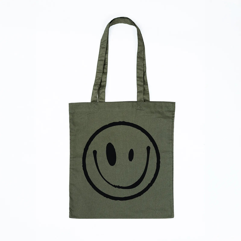 An olive green canvas tote bag with a large black hand-drawn smiley face printed on the front, set against a plain white background.