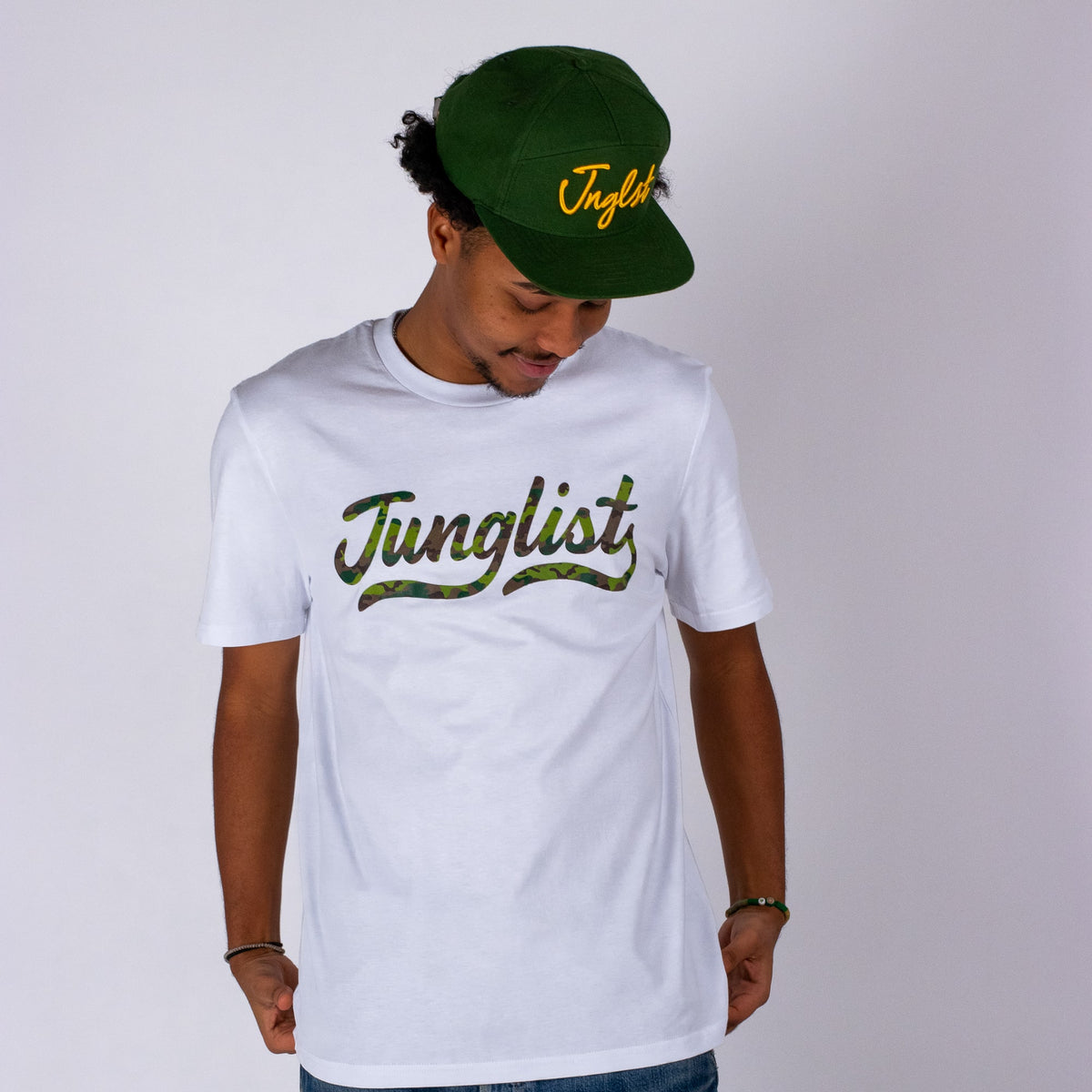 Person wearing a white t-shirt with 'Junglist' text and a green cap on a plain background